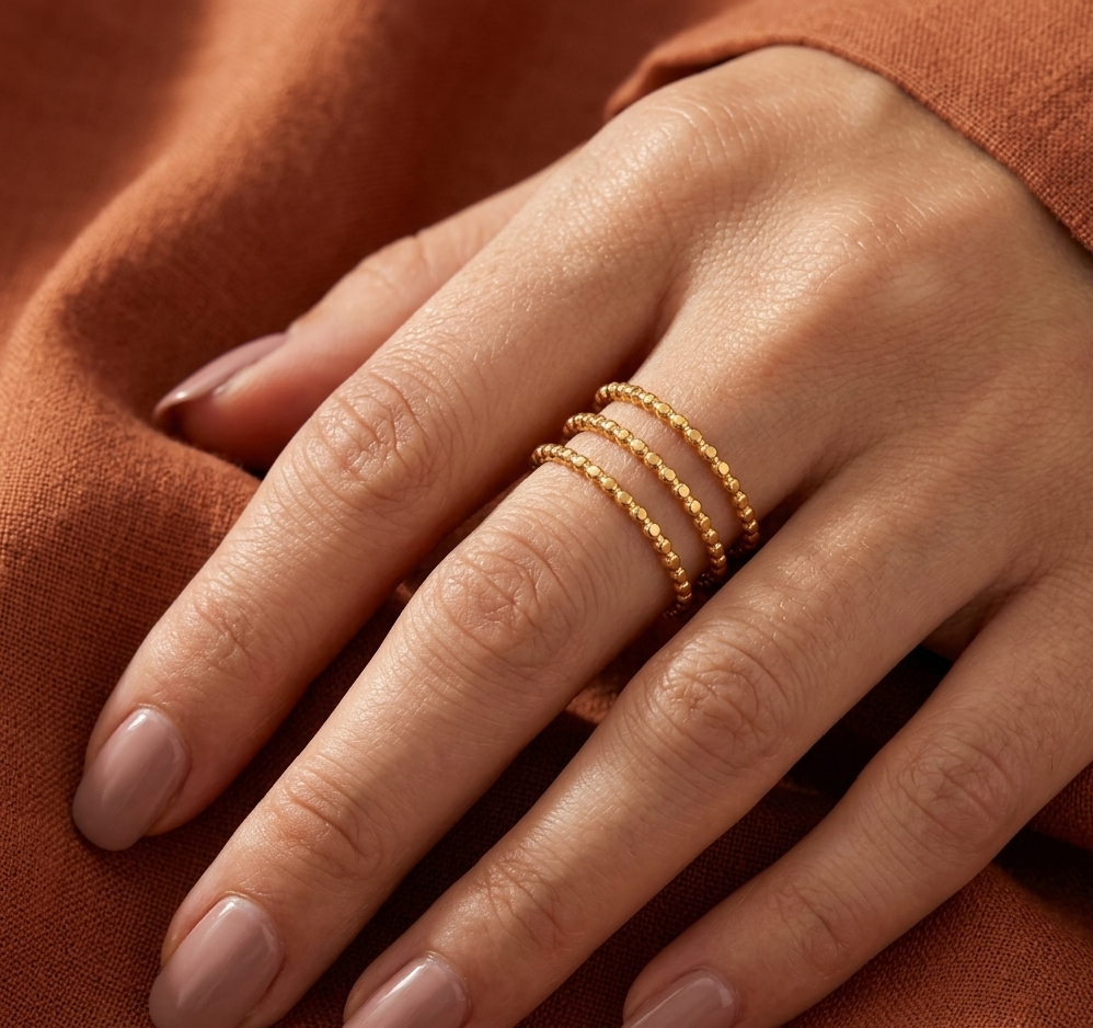 Close-up of a hand wearing gold rings on an orange fabric background