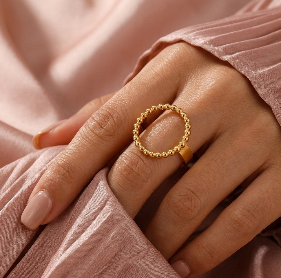 Gold ring on a hand with pink fabric background