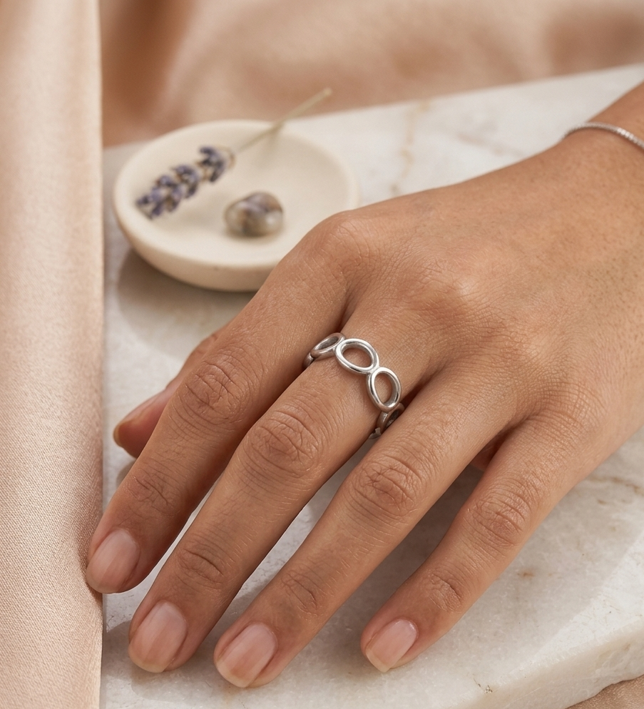 Hand wearing a silver infinity ring on a neutral background