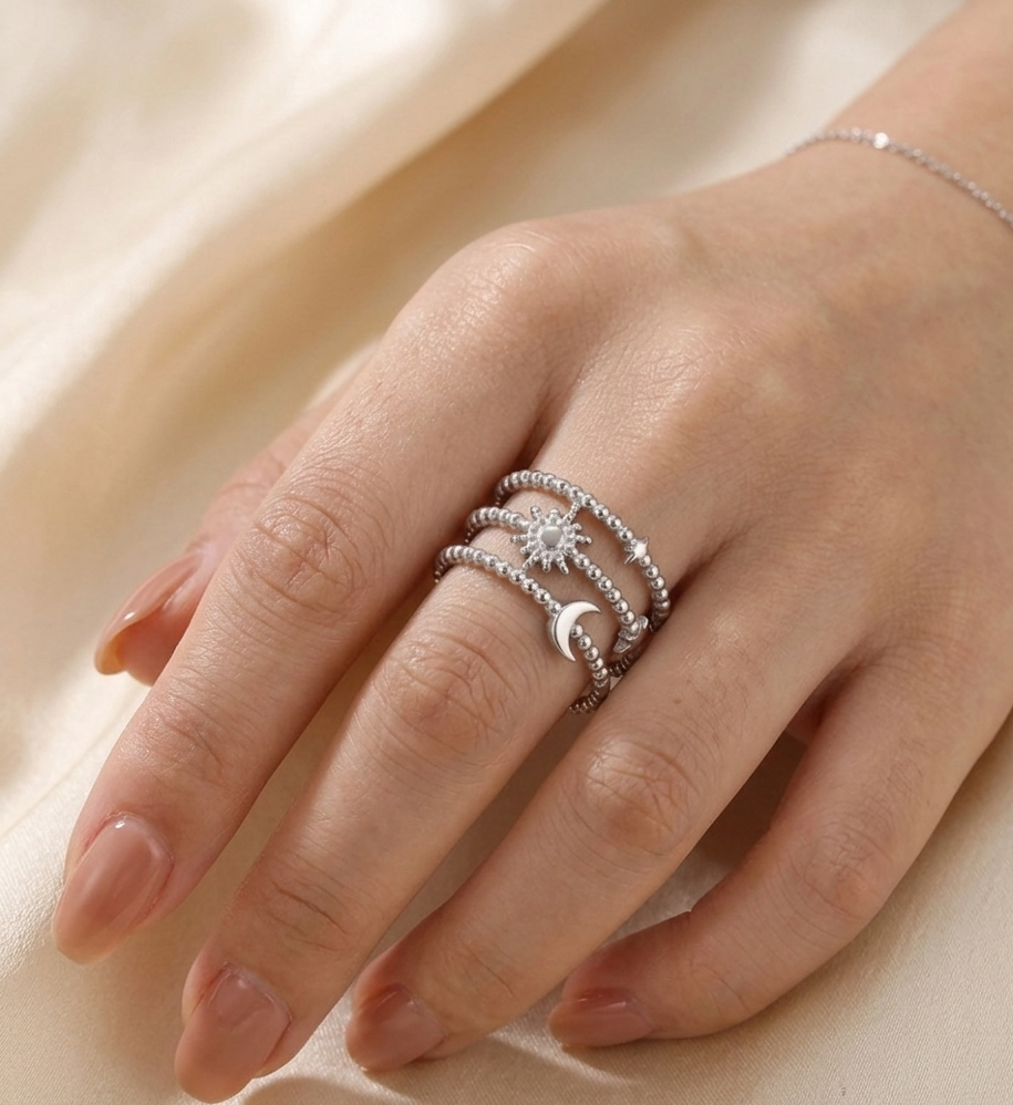 Hand wearing a stack of silver rings with a star and moon design on a beige fabric background