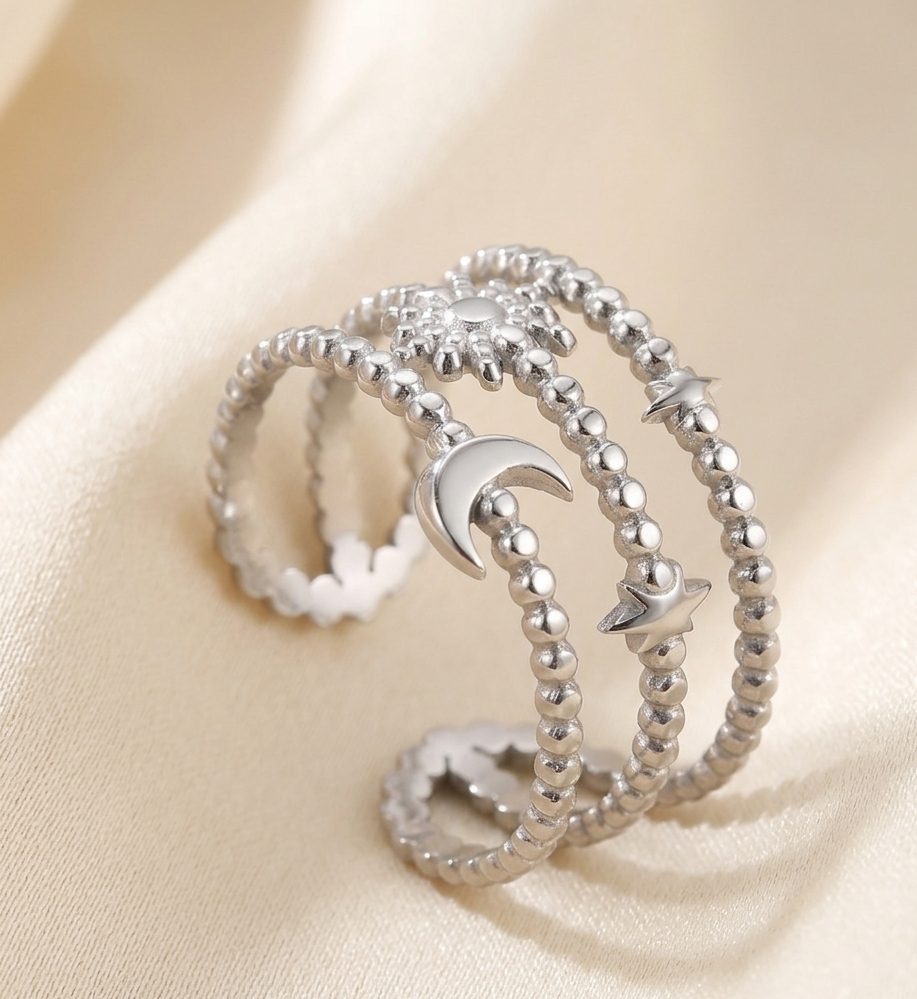 Three silver rings with moon and star designs on a beige fabric background