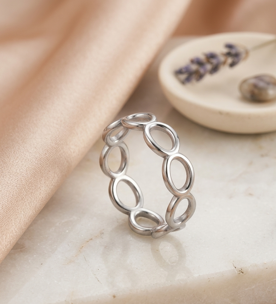 Silver ring with interlocking loops on a marble surface with a soft pink fabric background