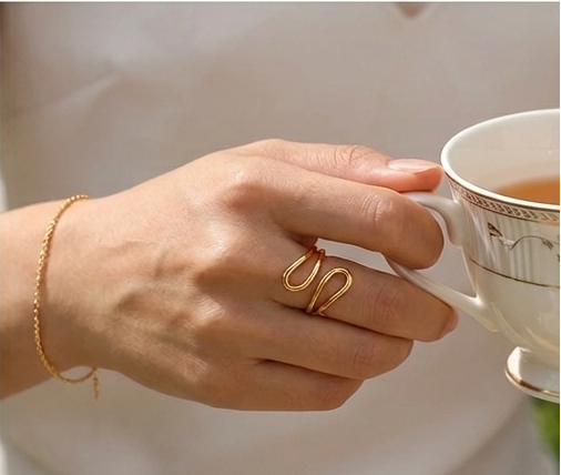 Gold ring on a marble surface with a cup of tea and flowers in the background