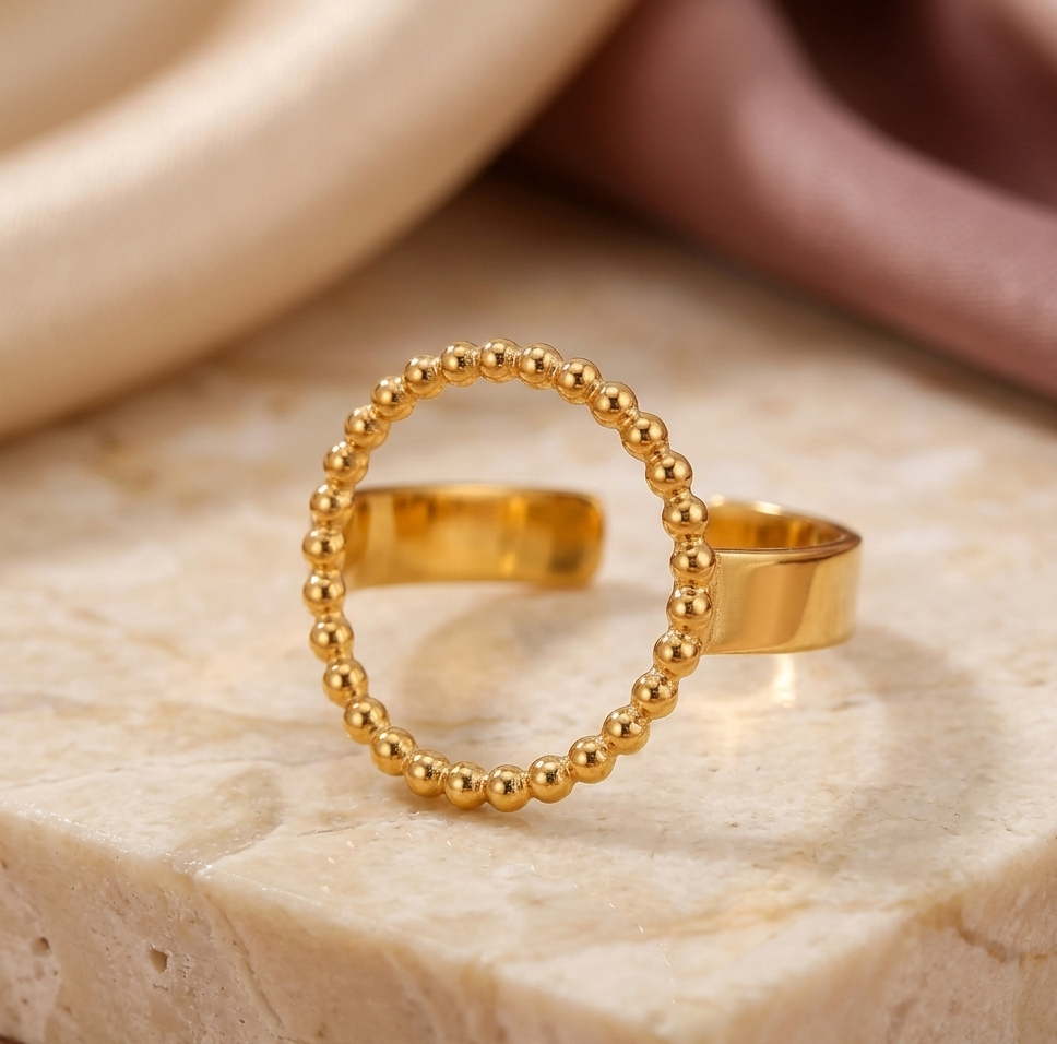 Gold beaded ring on a textured beige surface