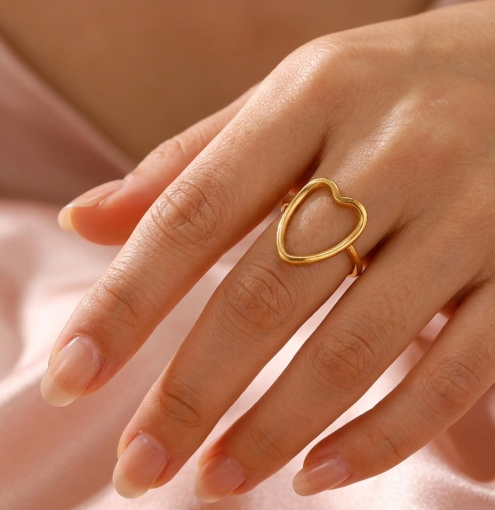 Gold heart-shaped ring on a hand against a soft pink background