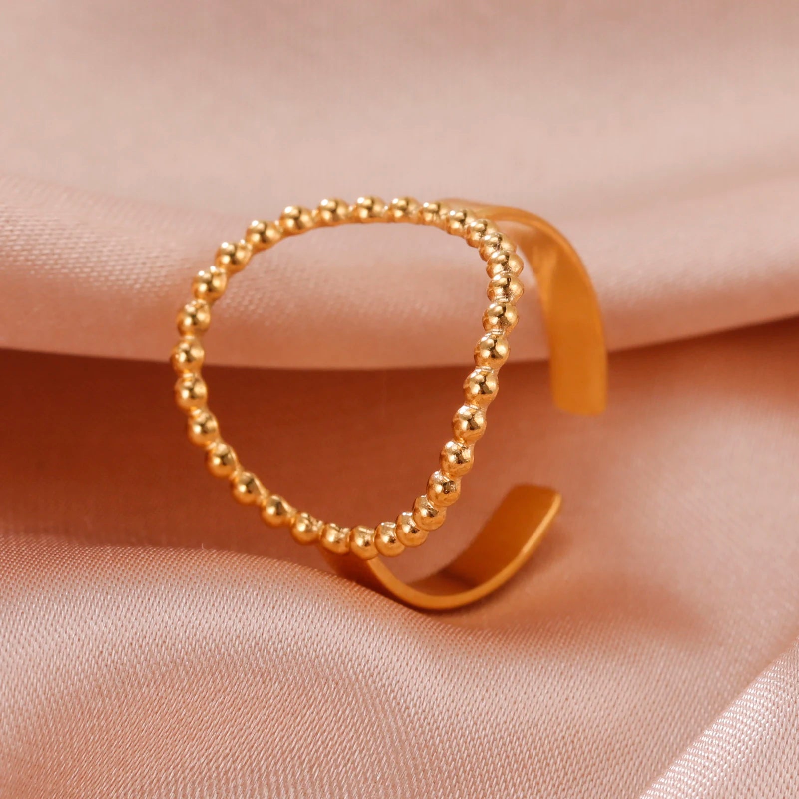 Gold open cuff ring on a soft pink fabric background