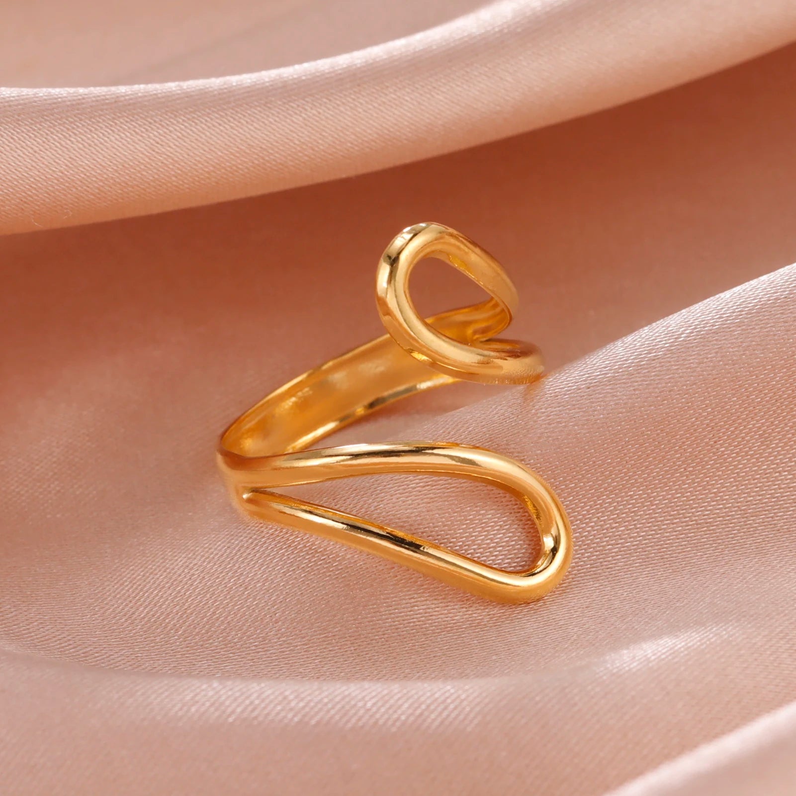 Gold ring with a modern design on a soft pink fabric background