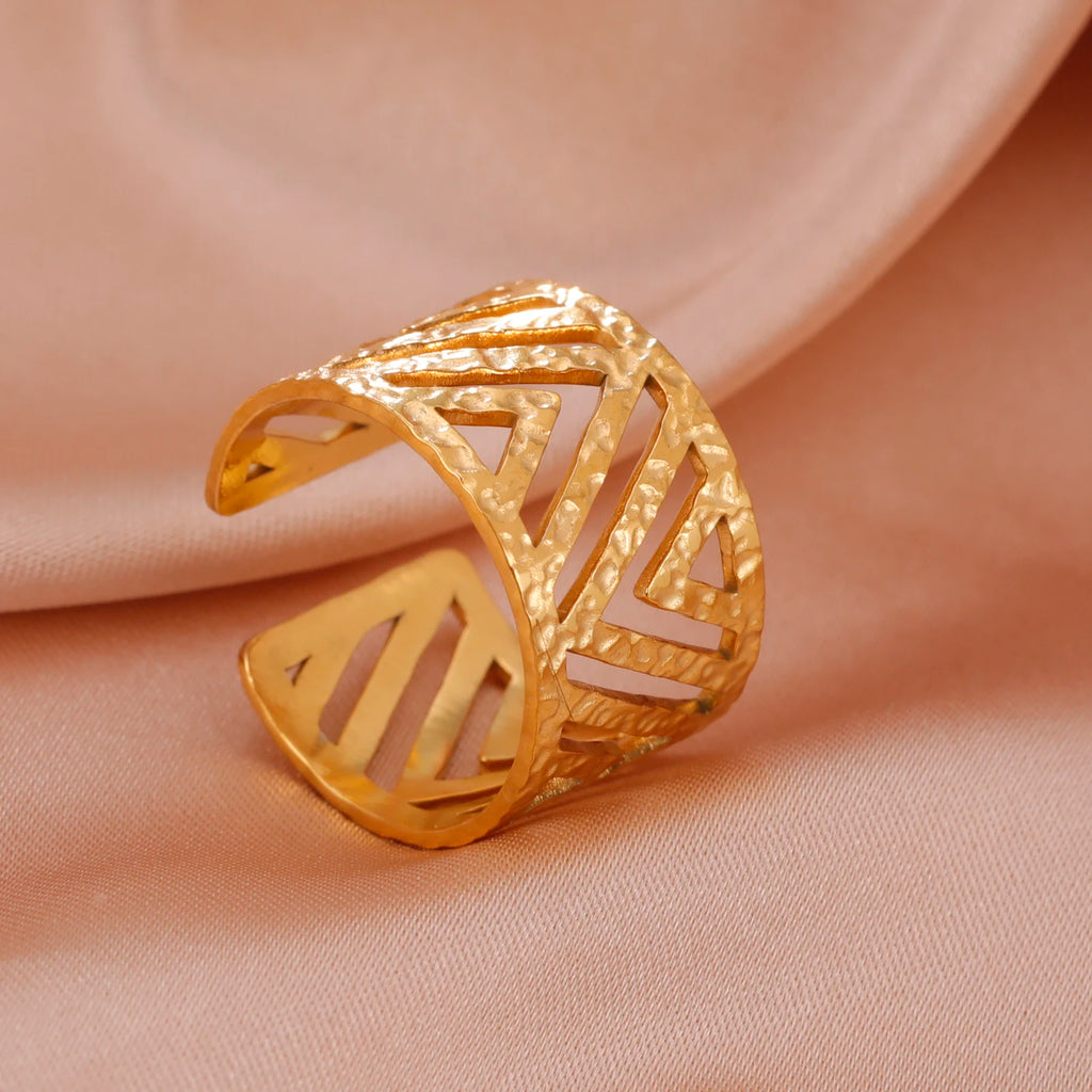 Gold ring with geometric design on a beige fabric background
