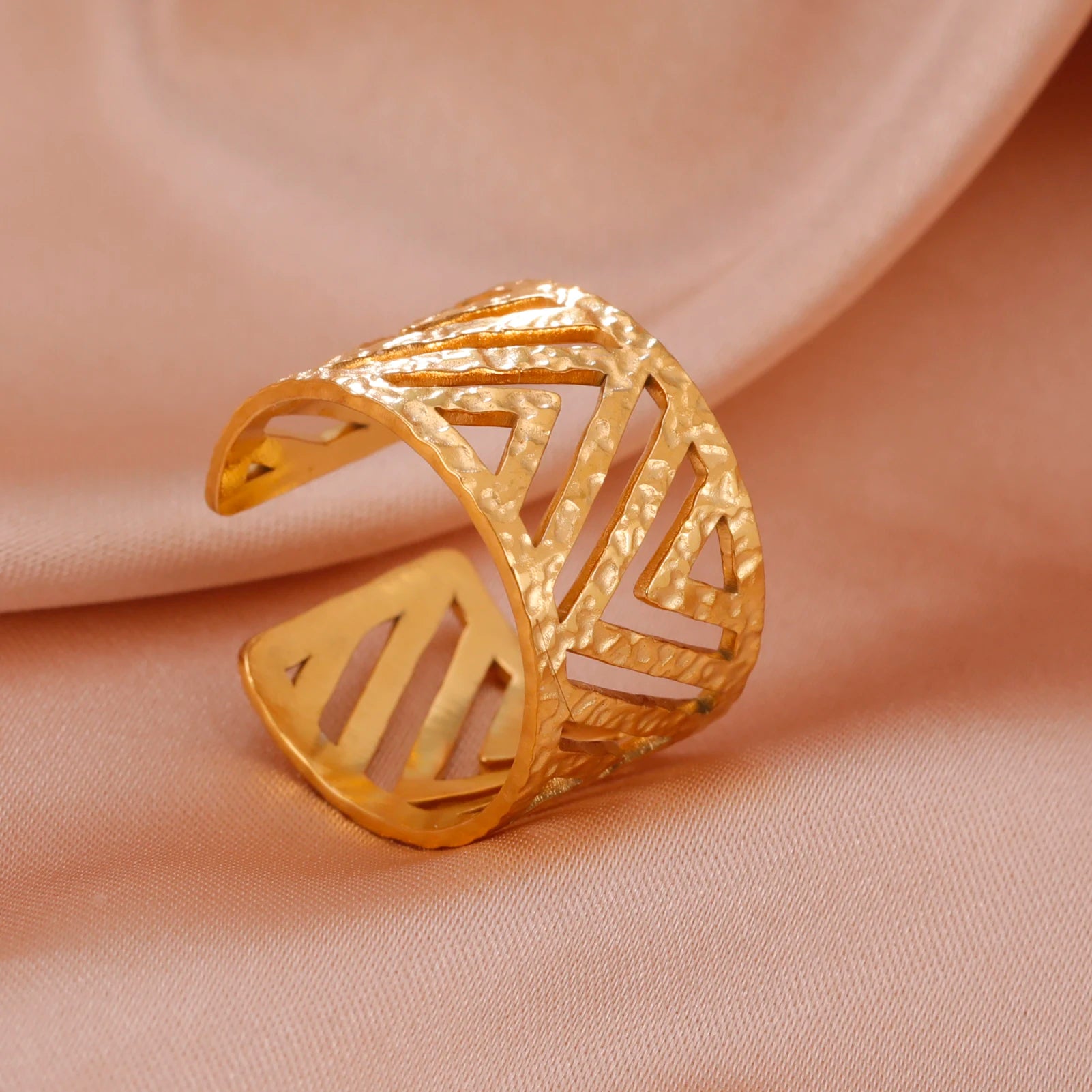 Gold ring with geometric design on a beige fabric background