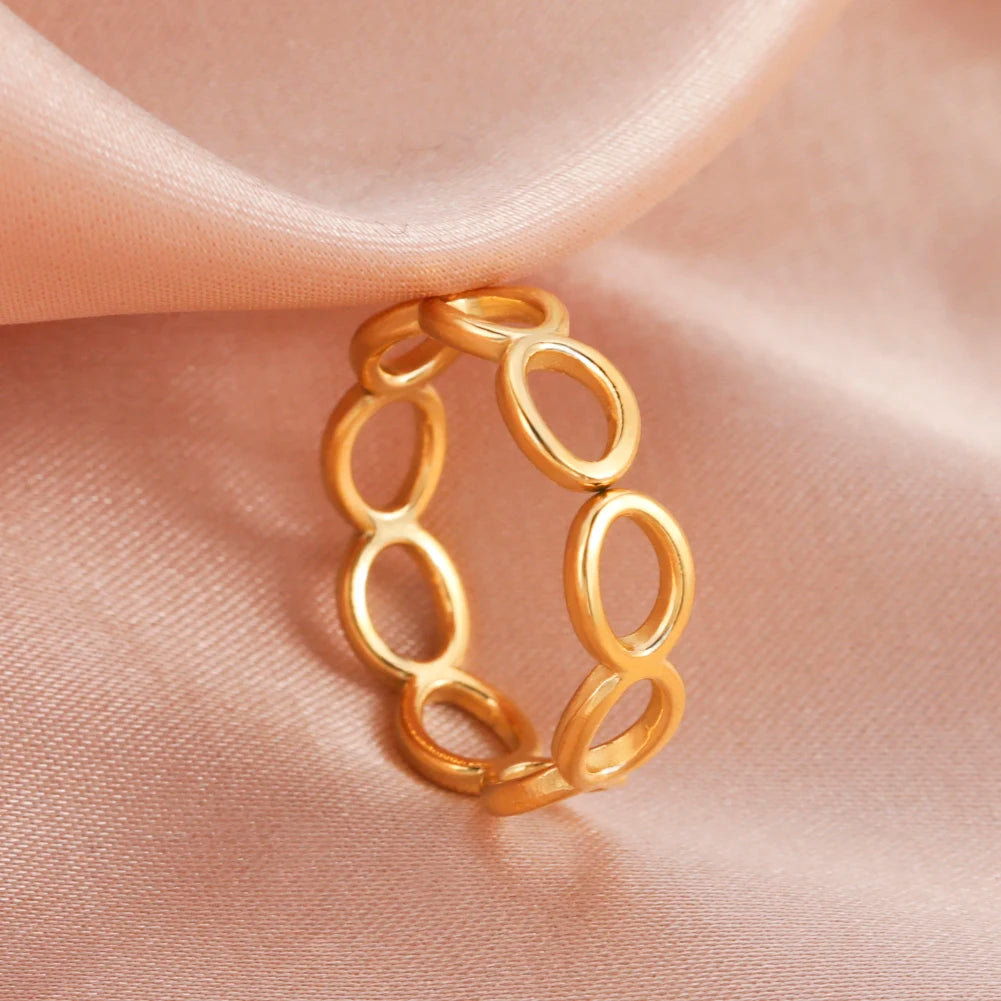 Gold ring with interlocking loops on a soft pink fabric background