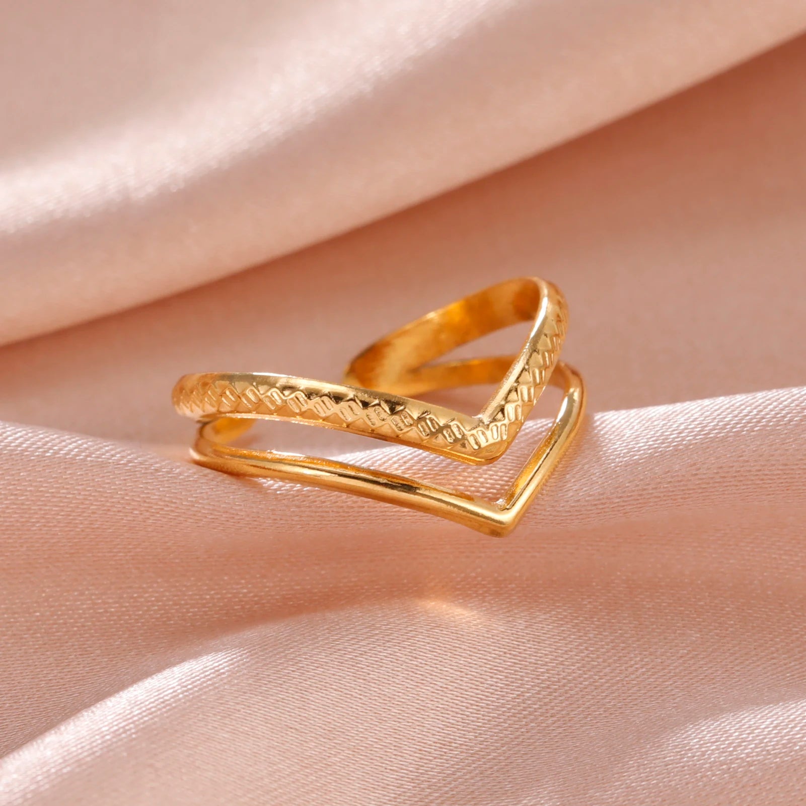 Gold ring with textured design on a soft pink fabric background