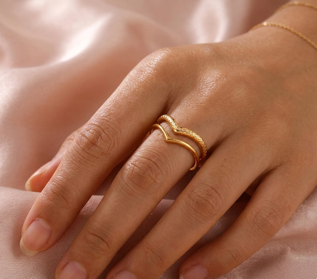 Hand wearing a gold ring on a soft pink fabric background