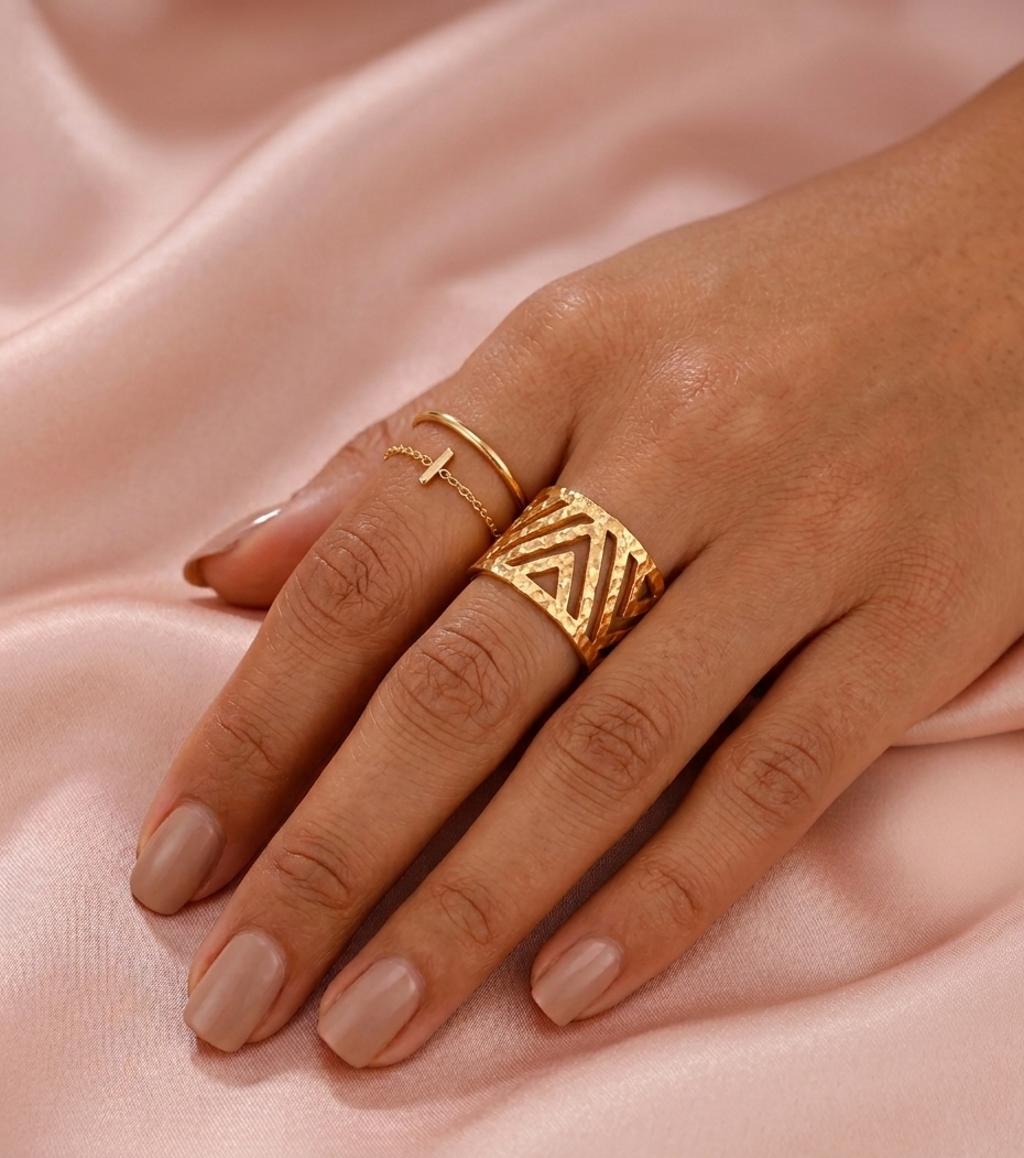 Hand wearing gold rings on a pink fabric background