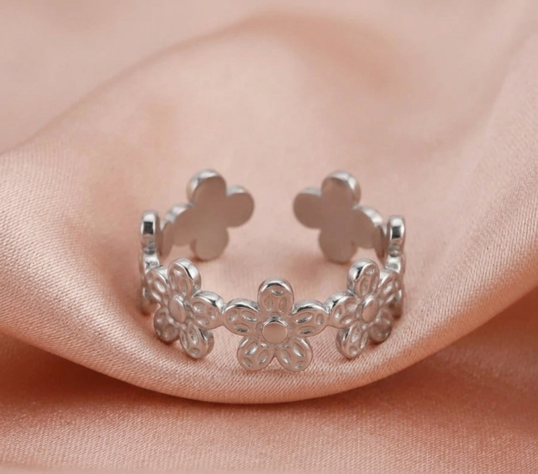 Silver adjustable ring with floral designs on a pink fabric background