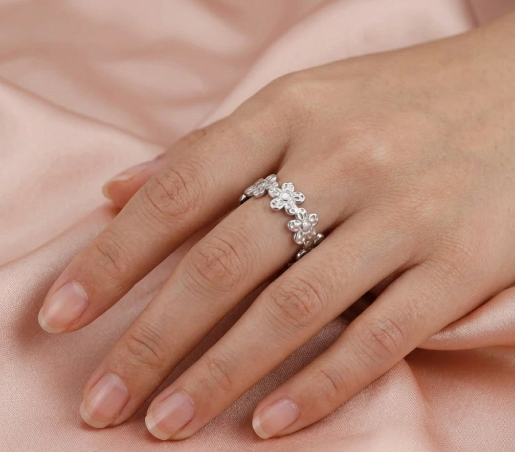 Silver ring with floral design on a hand against a soft pink background