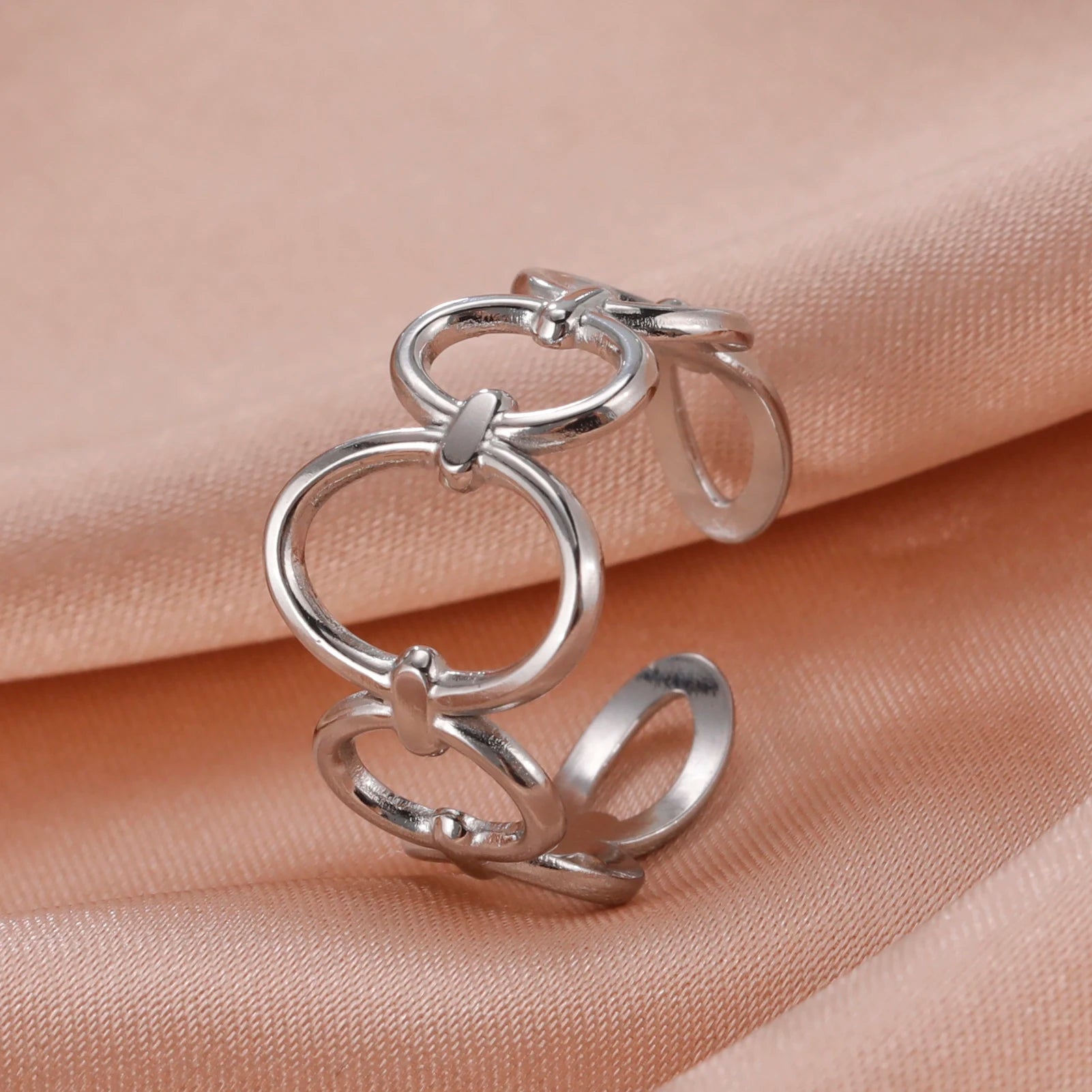 Silver ring with interlocking loops on a beige fabric background