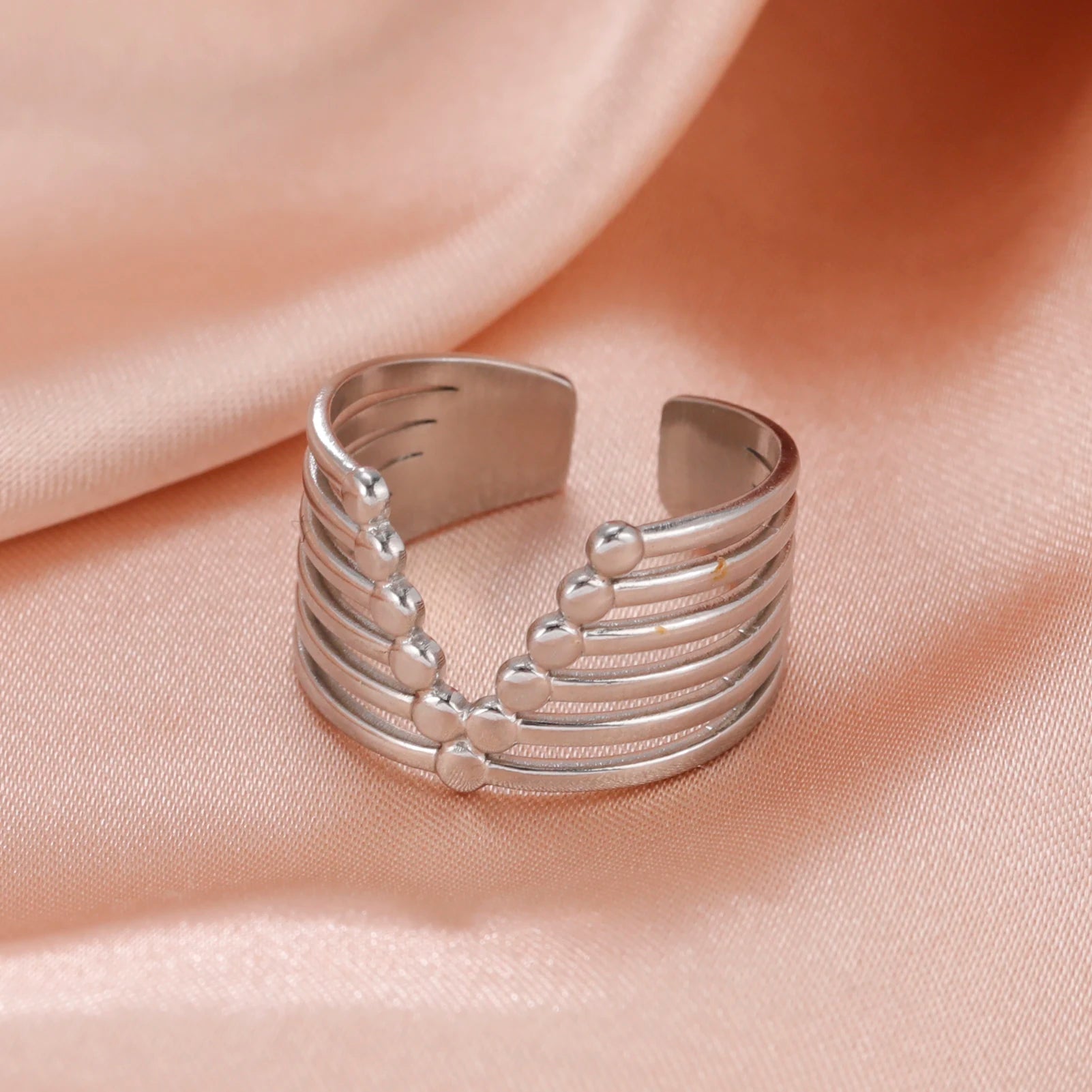 Silver ring with textured design on a soft pink fabric background