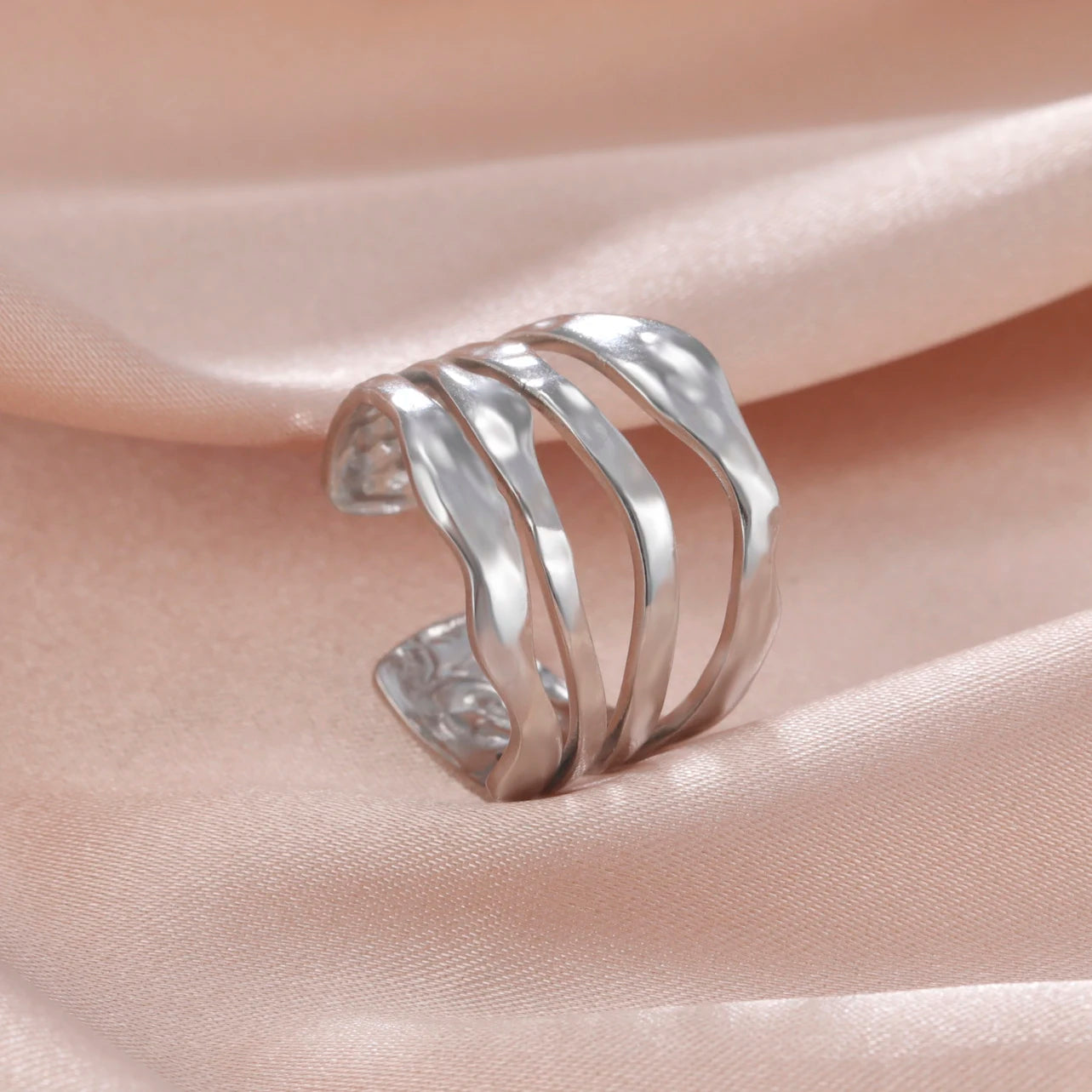 Silver ring with wavy design on a beige satin background