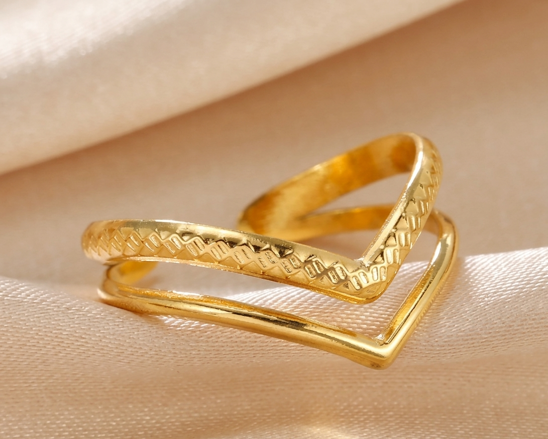 Two gold rings with textured design on a beige fabric background
